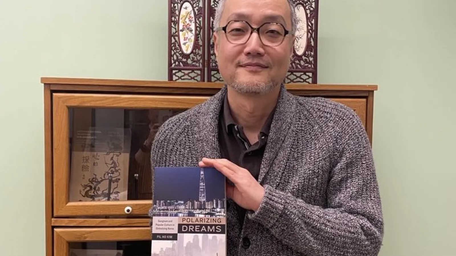 Person holding a book titled "Polarizing Dreams" in front of a wooden bookcase.