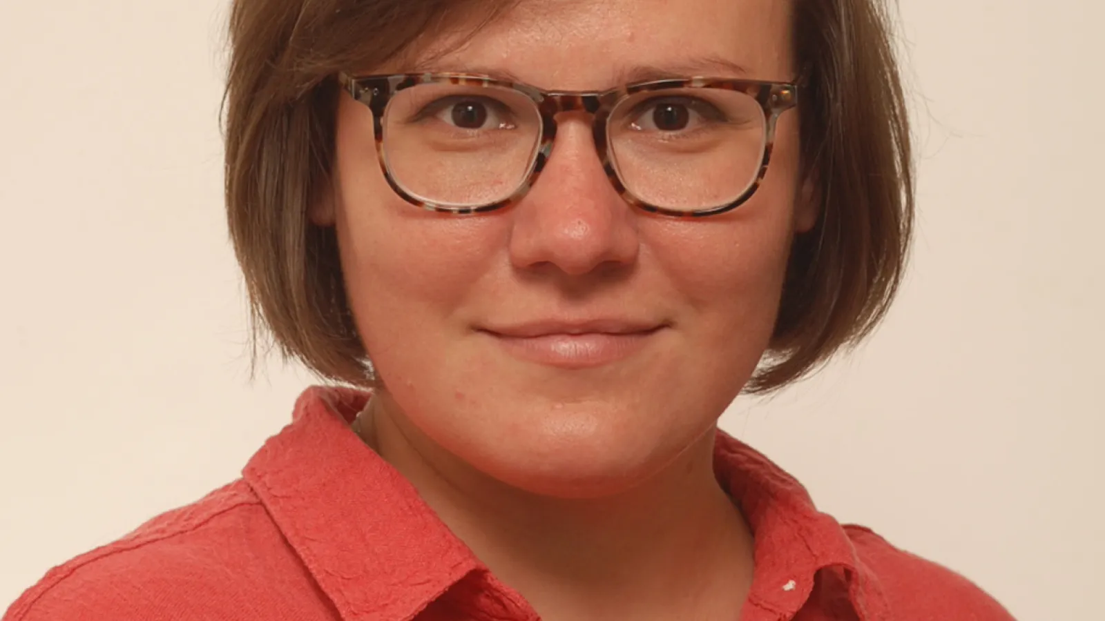 A woman wearing glasses and a red shirt, smiling and looking towards the camera. 