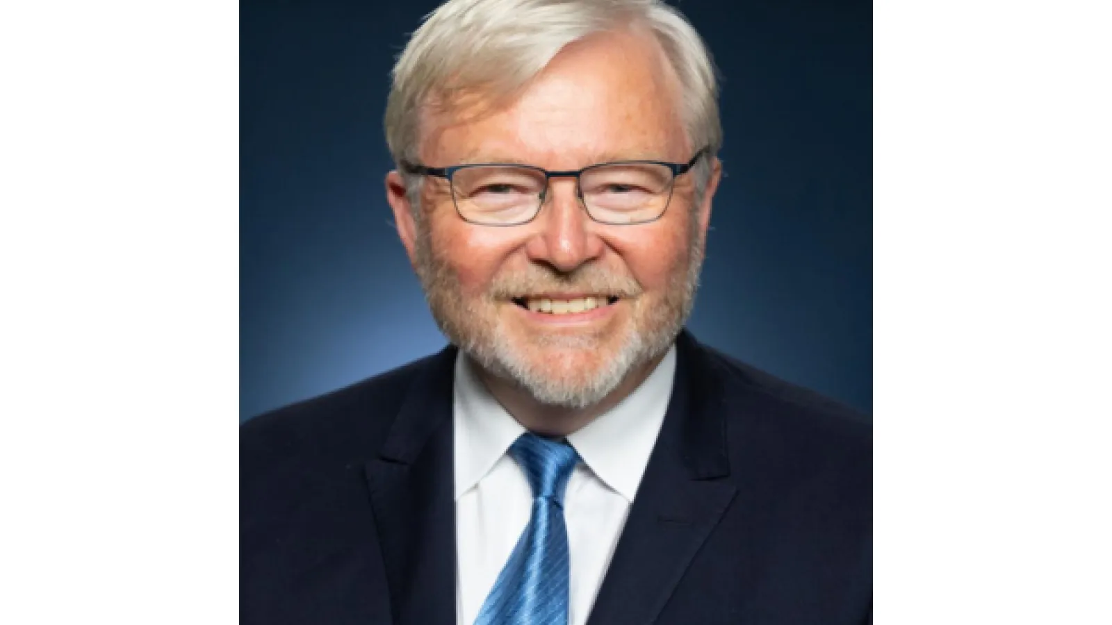 His Excellency the Honorable Kevin Rudd AC, older gentleman with glasses, trimmed beard, in a navy suit and blue tie.