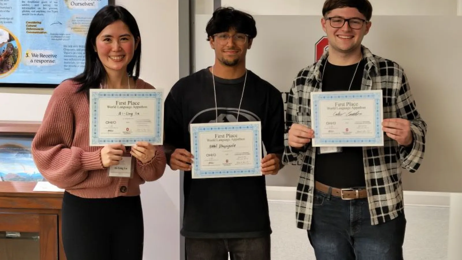 Three students pose with their certificates in front of a wall, smiling with pride