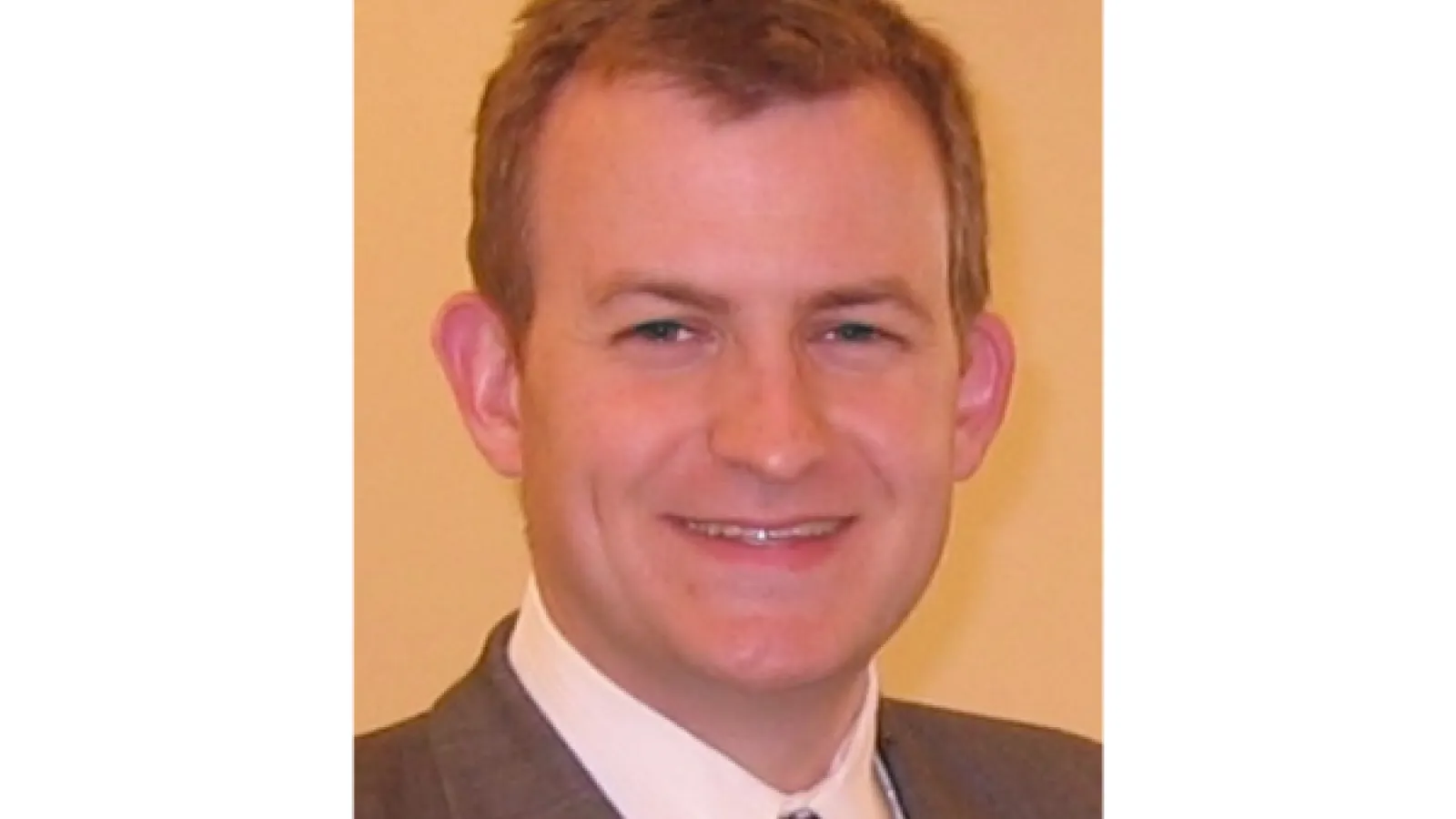 Rob Kelly, a light brunette man in a grey suit smiling for a headshot. 