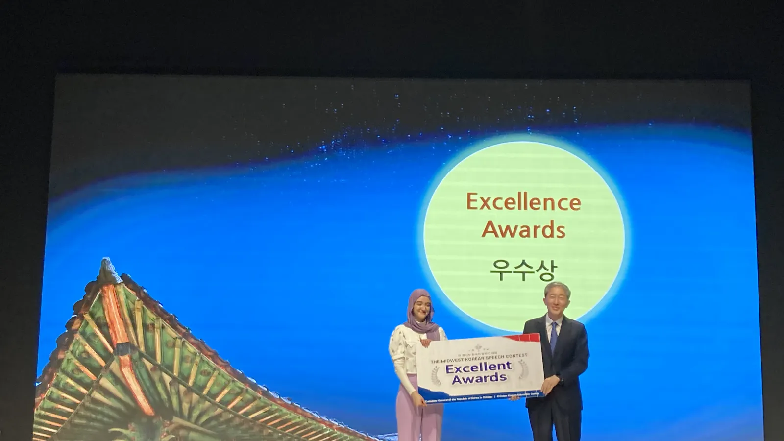 Young woman is presented award from older man on a stage
