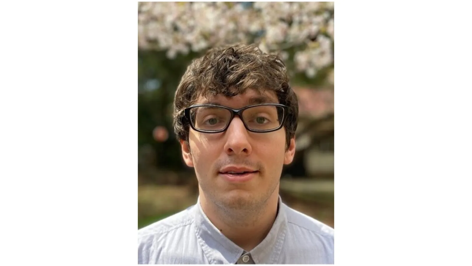 Man with dark curly hair and glasses looks toward the camera