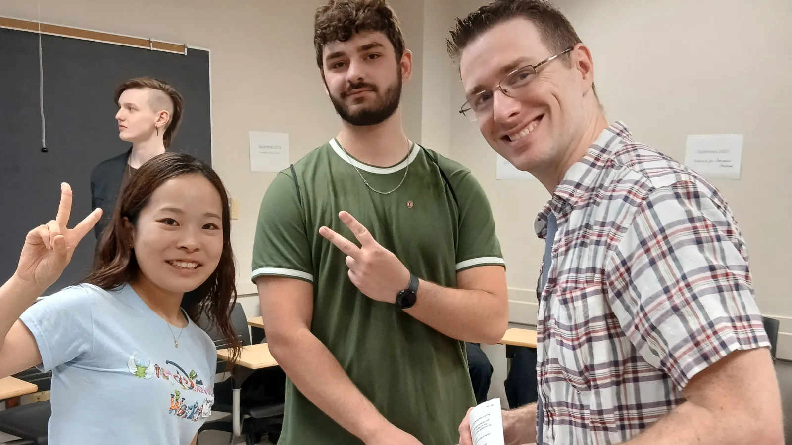 1 woman (left) and 2 men posed with smiles in a classroom