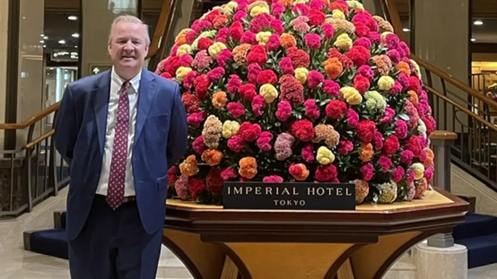 Man with the blue suit and a red tie standing next to an exceptionally large flower bouquet