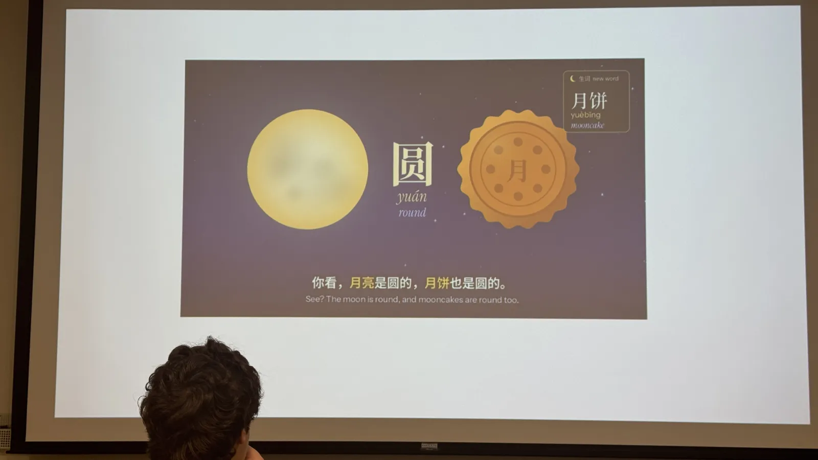 Projected language-learning slide showing a full moon, a mooncake, and text explaining that both are round.