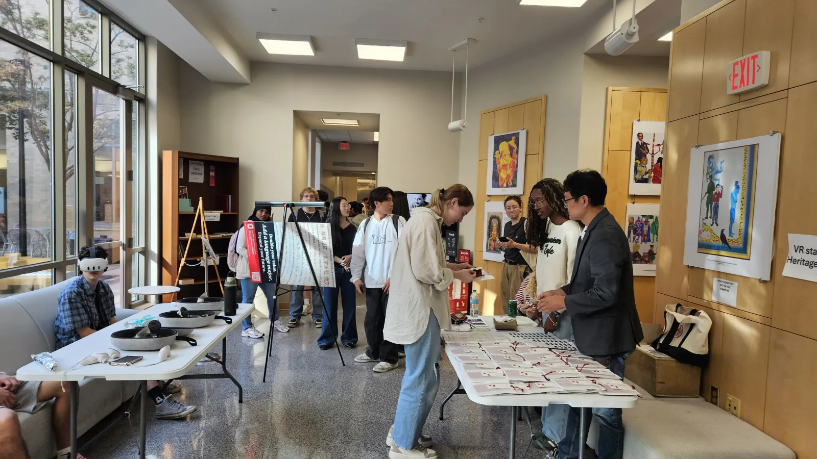Students at an information desk with other students wearing virtual reality headsets in the background