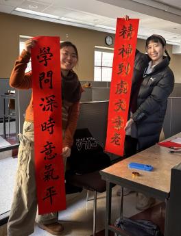 Two individuals display two red banners, showcasing a message in a lively environment