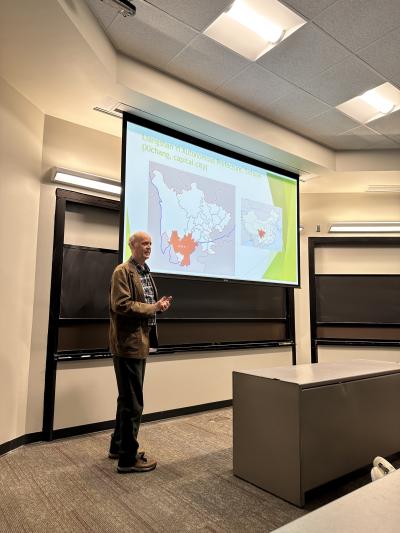 A man stands in front of a large projection screen, preparing to present information to an audience.  