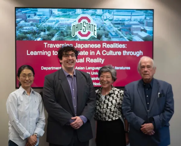 four individuals stand before a large screen displaying "Transforming Japanese Realities: Learning Through Culture."