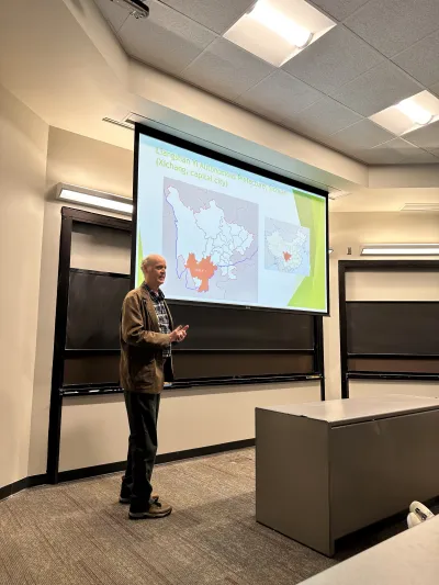 A man stands in front of a large projection screen, preparing to present information to an audience.  