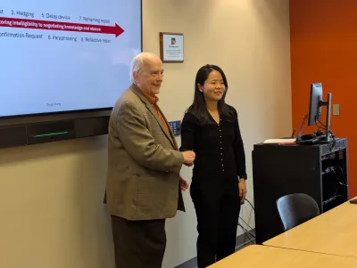 A man and woman shaking hands in front of a large presentation screen, symbolizing agreement or collaboration