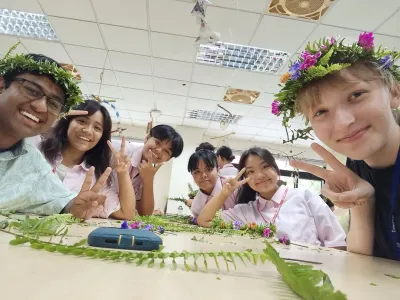 A group of young people smiling and posing for a photo, each wearing floral headpieces. 