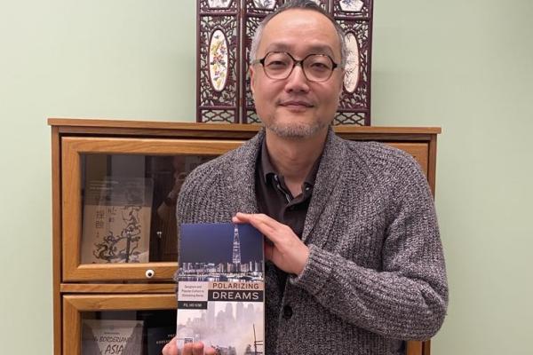 Person holding a book titled "Polarizing Dreams" in front of a wooden bookcase.