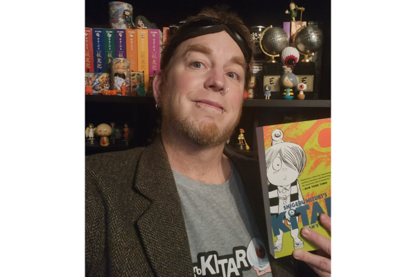 A man holds a book aloft, showcasing a vibrant cartoon character illustrated on the front.