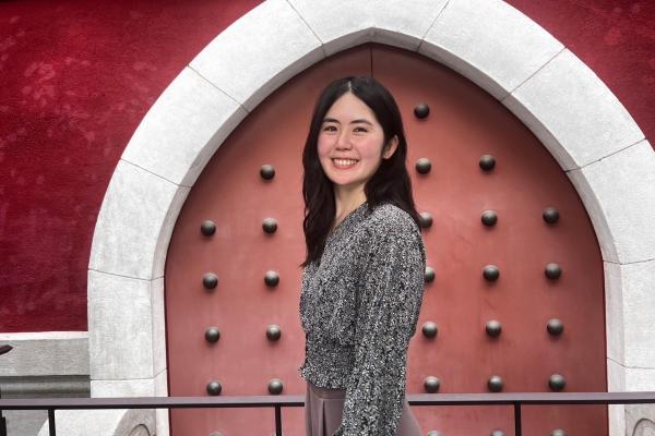 A woman smiles while standing in front of a large, red, studded door set in an archway with a dark red wall.