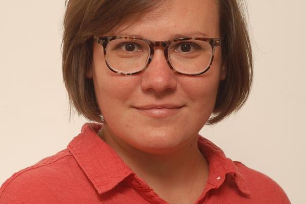 A woman wearing glasses and a red shirt, smiling and looking towards the camera.