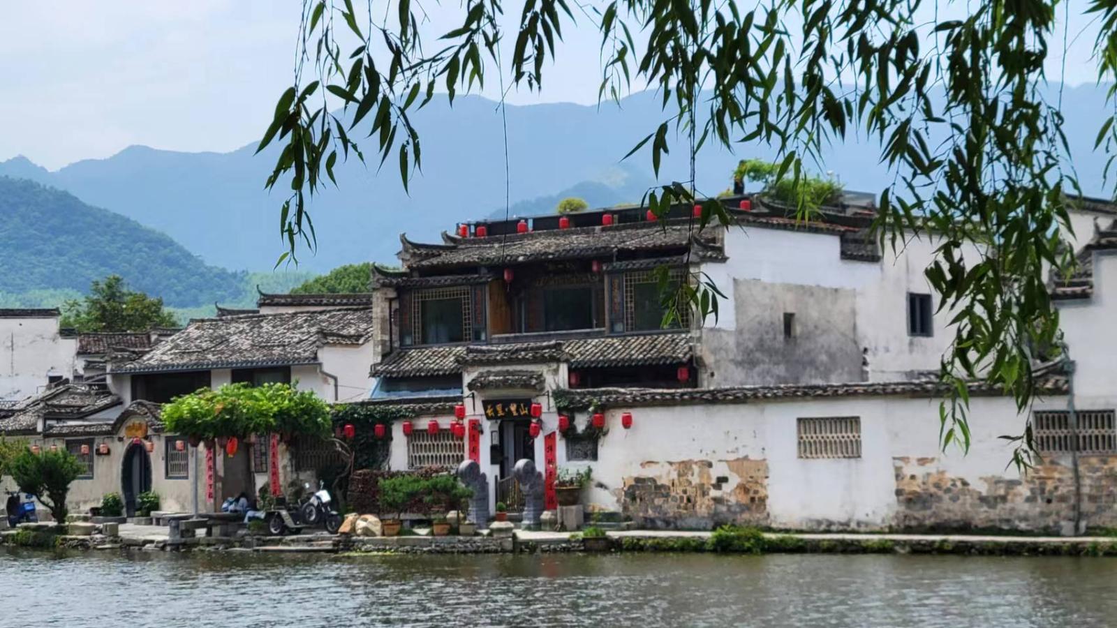 A scenic river in China, flanked by modern buildings and lush green trees along its banks. 
