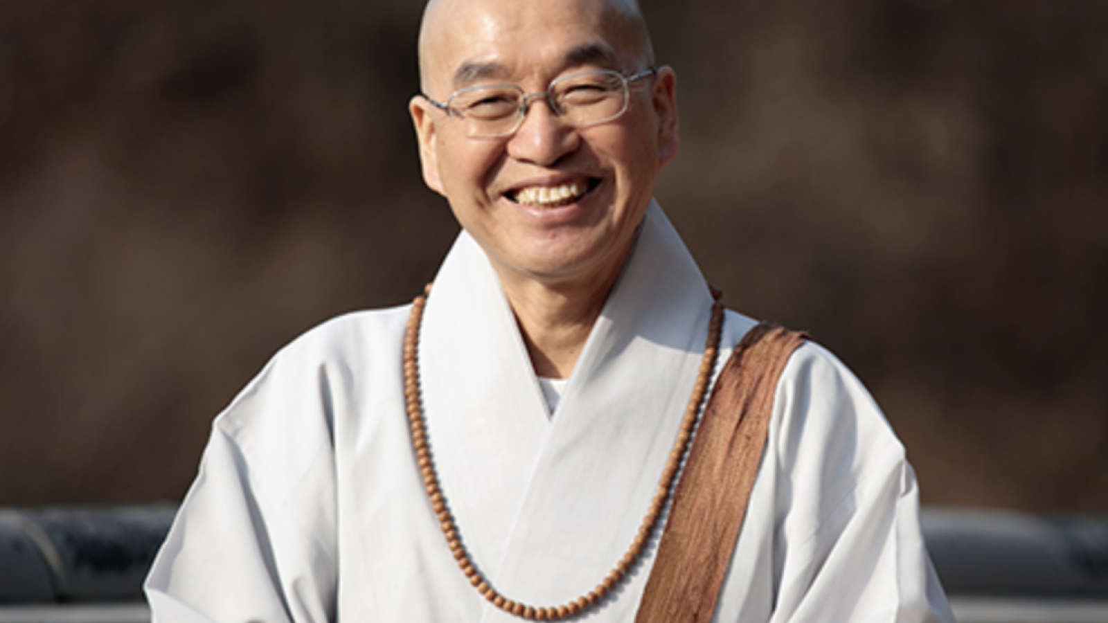 Man wearing buddhist monks robe and rosary smiling at camera