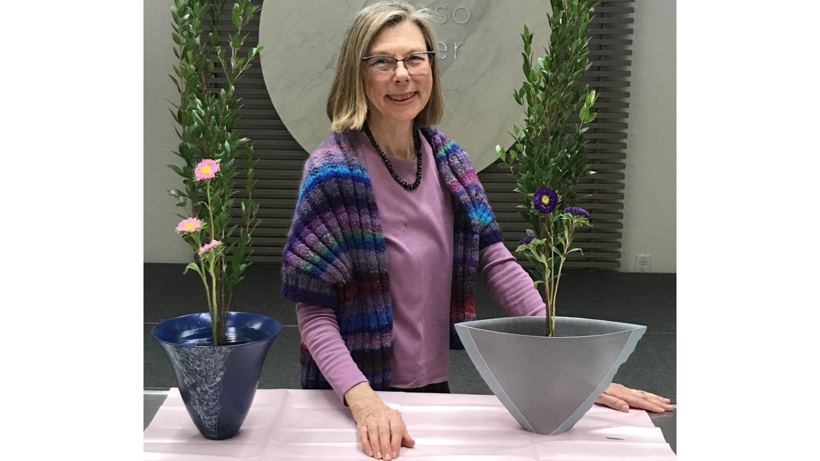 Woman in a colorful sweater smiling at atable with 2 flower vases