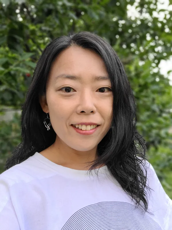 Woman with dark hair, smiling towards the camera with green trees in the background