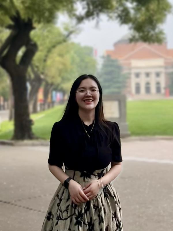 A woman in a skirt standing in front of a building (Yan Li)