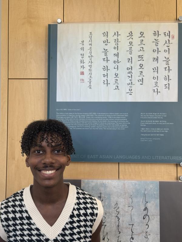 A smiling young man poses in front of a wall with Korean script, embodying joy and a connection to diverse cultures.