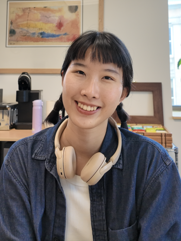 A young woman with headphones on, engaged in her tasks at a desk in a professional office setting.
