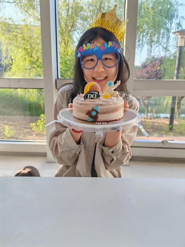 A girl with glasses and a crown joyfully holds a decorated cake, celebrating a special occasion.  