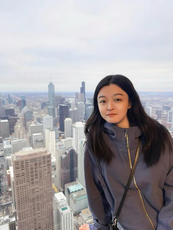  A woman stands on a ledge, gazing out over a sprawling cityscape under a clear blue sky. 