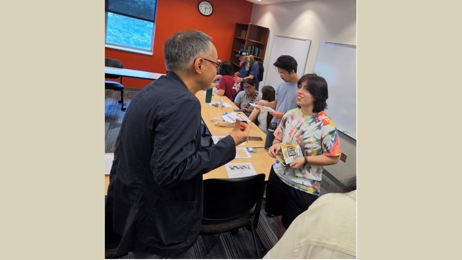 Professor talking to one student in foreground with more students in the background
